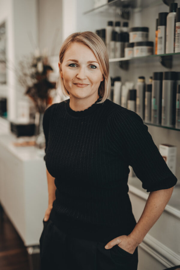 Lächelnde Inhaberin schaut direkt in die Kamera und strahlt Freundlichkeit aus.  